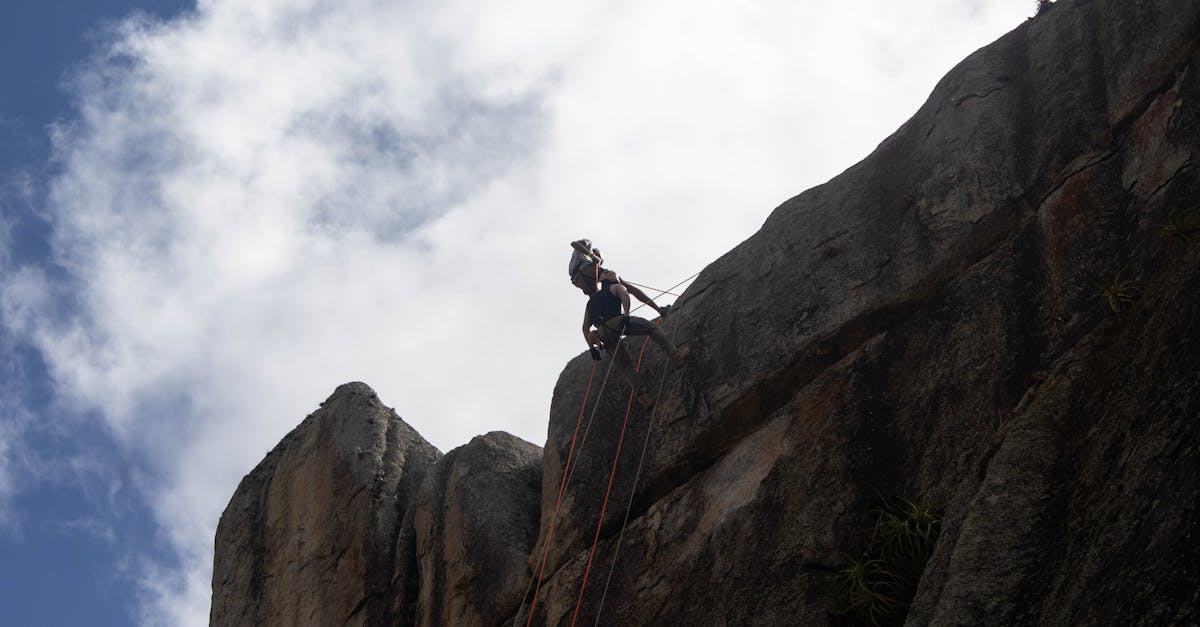 An adventurous rock climber scales a steep cliff under a bright sky, showcasing extreme sports courage.